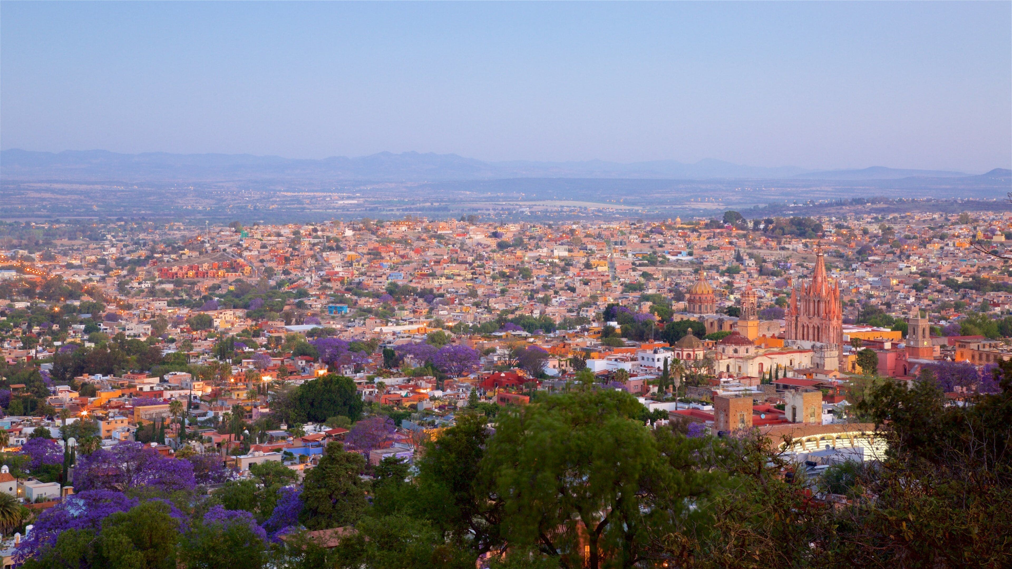 A cityscape with a prominent cathedral, dense urban buildings, and distant mountains.