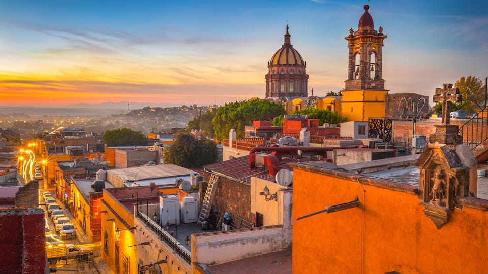 A cityscape with a prominent dome and bell tower, a busy street with cars, and a sunset sky.