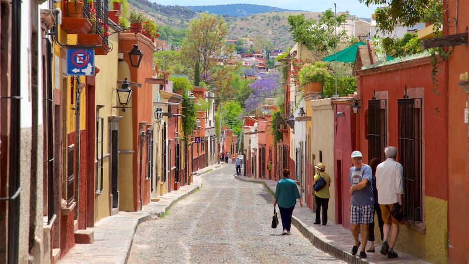 A cobblestone street lined with colorful buildings, a no parking sign, and people walking.