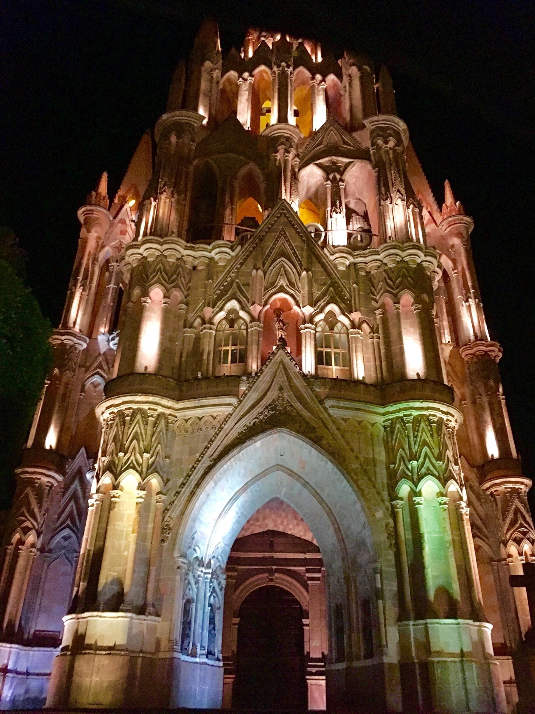 Una catedral de estilo gótico con detalles intrincados en piedra y ventanas iluminadas en la noche.