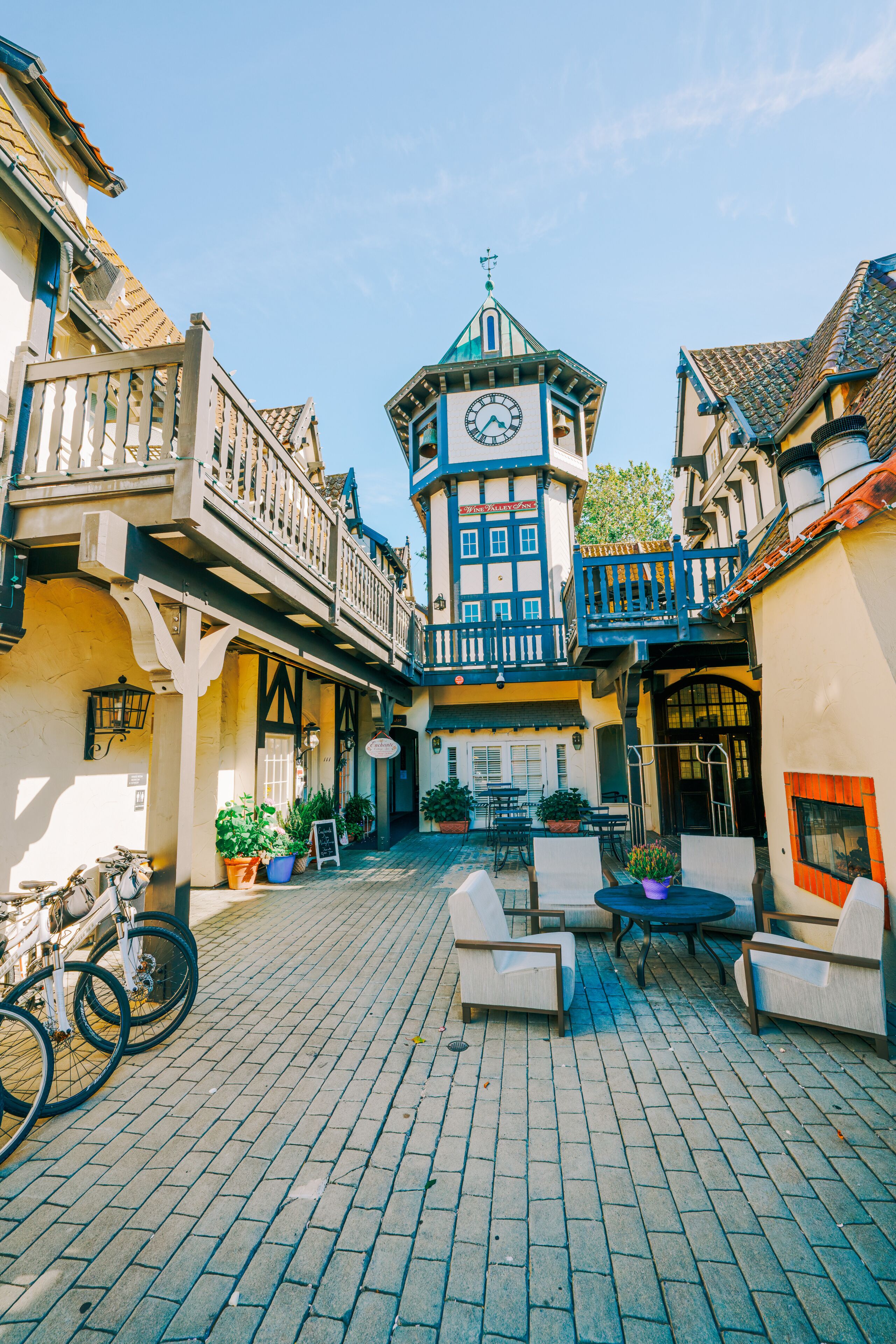 Un patio empedrado con una torre de reloj, mobiliario de exterior y una bicicleta.
