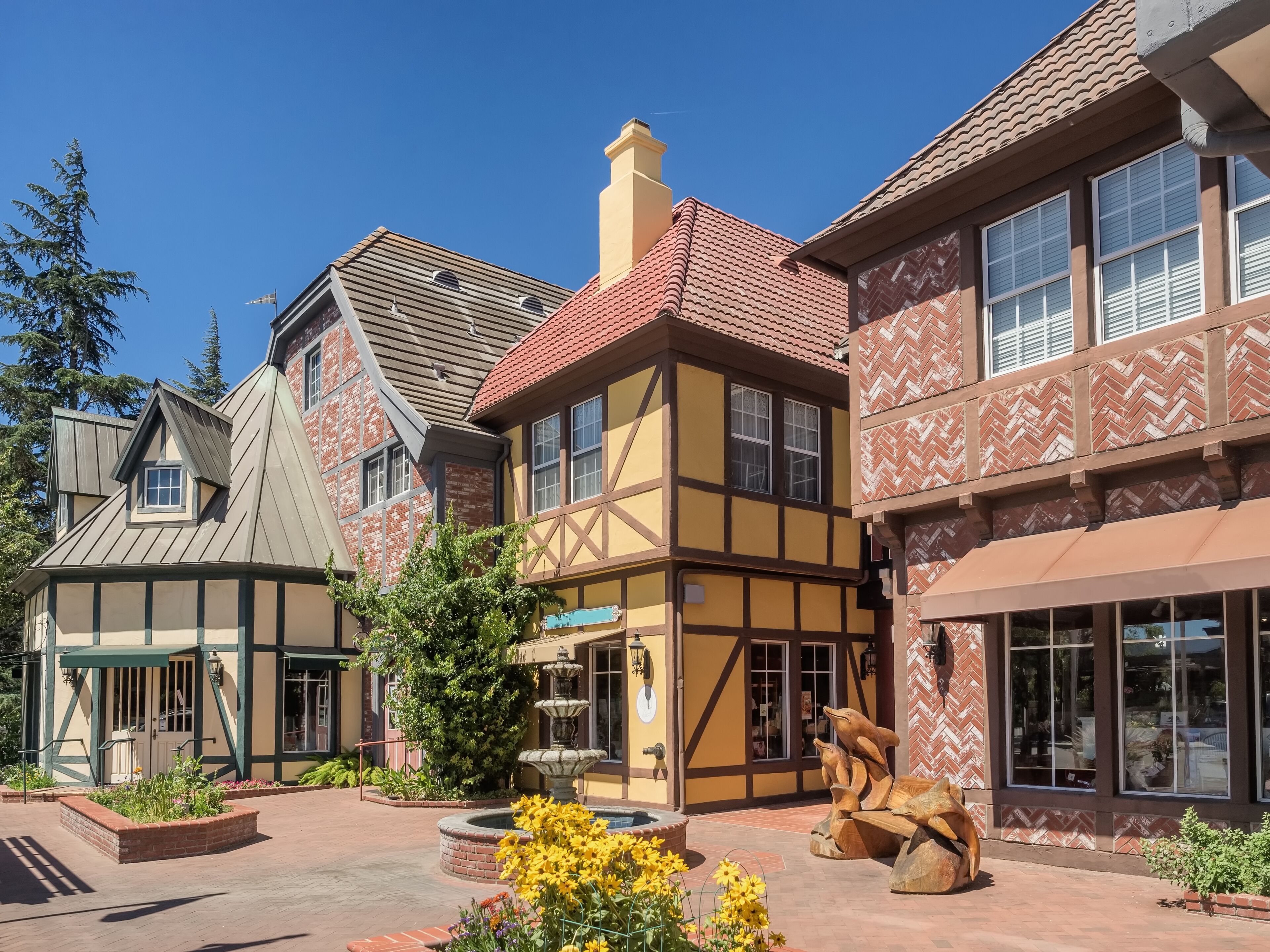 A courtyard with Tudor-style buildings, a fountain, and a wooden sculpture.