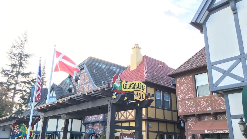 Un pueblo europeo tradicional con casas de entramado de madera, un cartel que dice 'Gledeliga Jul' y un letrero que indica 'Unique Shops'.