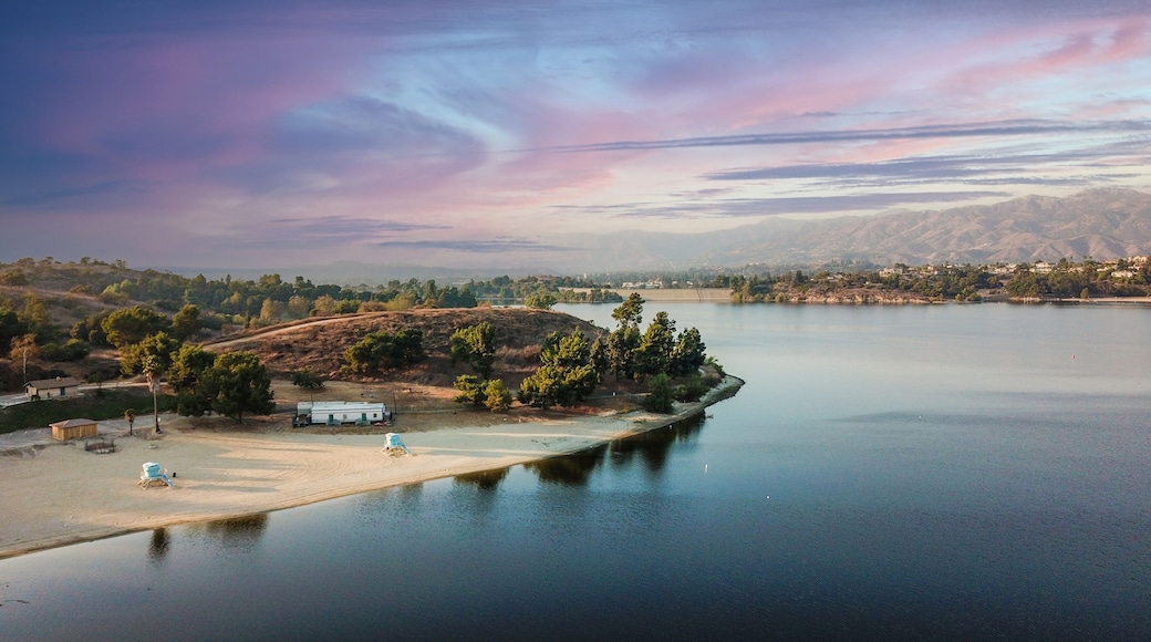 a stunning aerial shot of the still blue waters, the pier, the lush green trees and majestic mountain ranges at Puddingstone Lake in San Dimas California USA