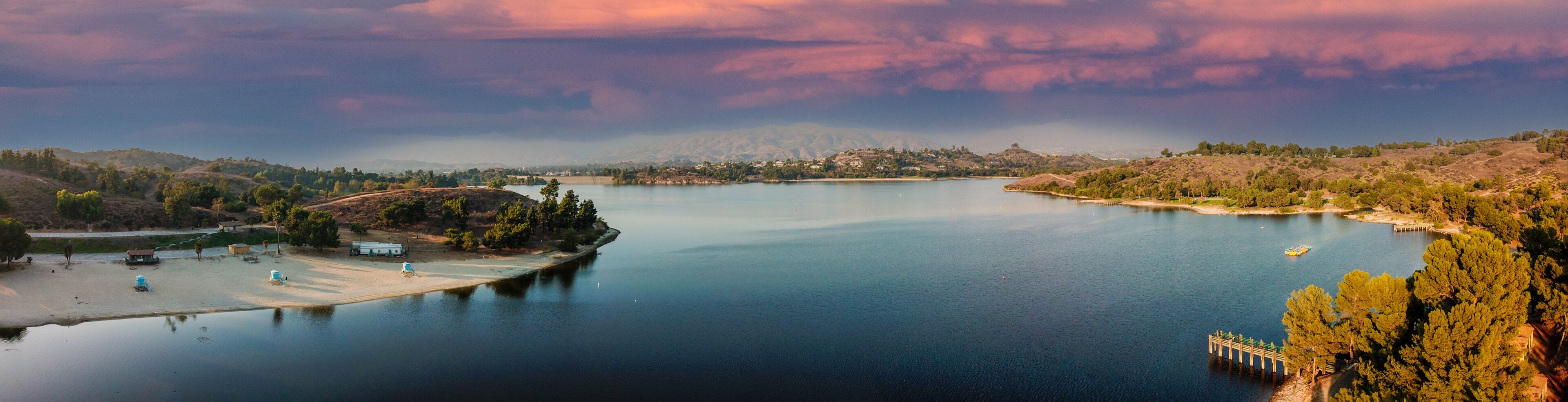 a breathtaking aerial panoramic shot of the still blue waters and lush green trees and majestic mountain ranges at Frank G Bonelli Regional Park at Puddingstone Lake in San Dimas California
