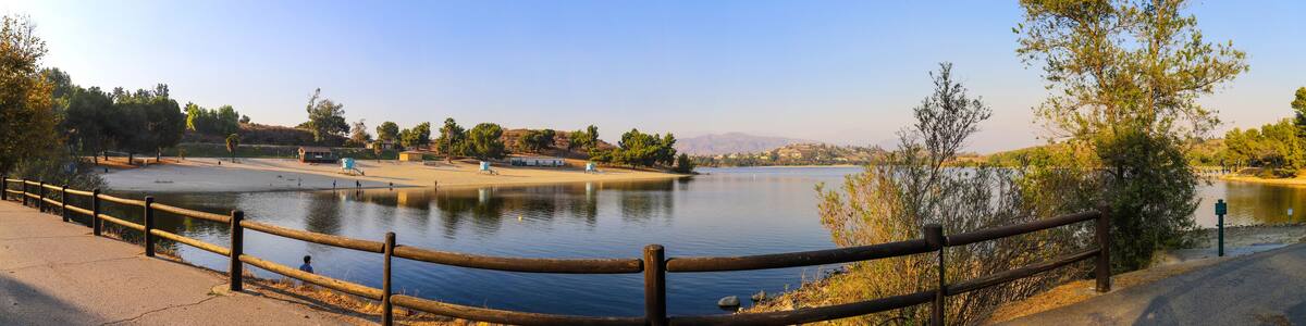 a breathtaking panoramic shot of the still blue waters and lush green trees and majestic mountain ranges at Frank G Bonelli Regional Park at Puddingstone Lake in San Dimas California USA