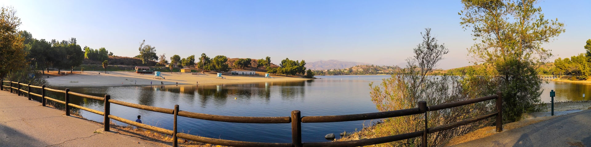 a breathtaking panoramic shot of the still blue waters and lush green trees and majestic mountain ranges at Frank G Bonelli Regional Park at Puddingstone Lake in San Dimas California USA