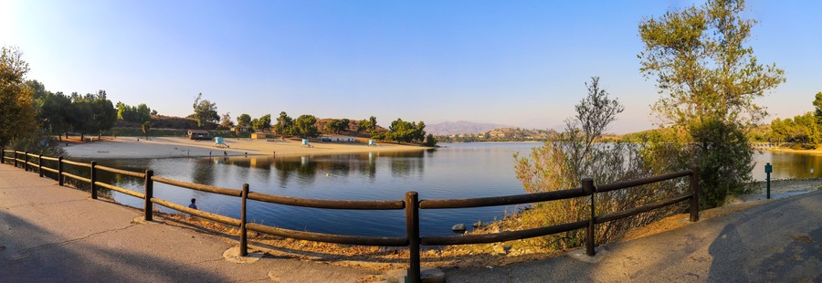 a breathtaking panoramic shot of the still blue waters and lush green trees and majestic mountain ranges at Frank G Bonelli Regional Park at Puddingstone Lake in San Dimas California USA