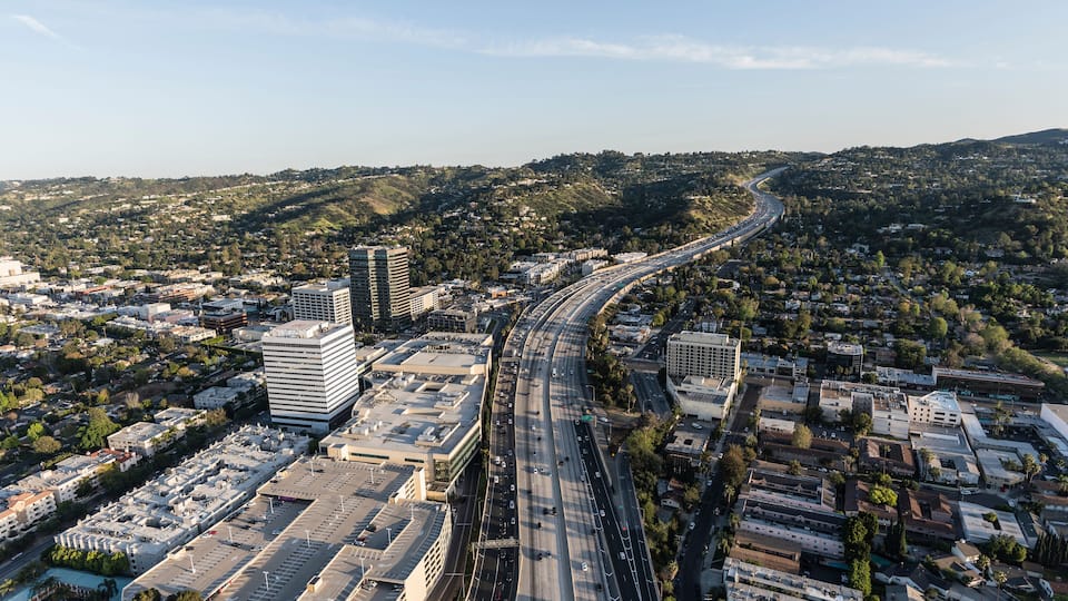 A cityscape with a prominent highway curving through it, surrounded by buildings and hills.