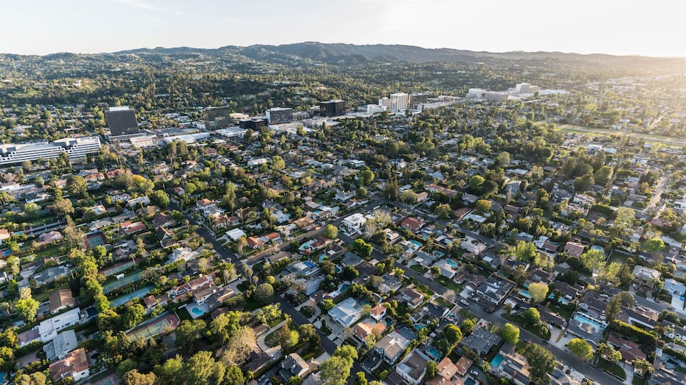 An aerial view of a residential area with houses, trees, and a distant mountain range.