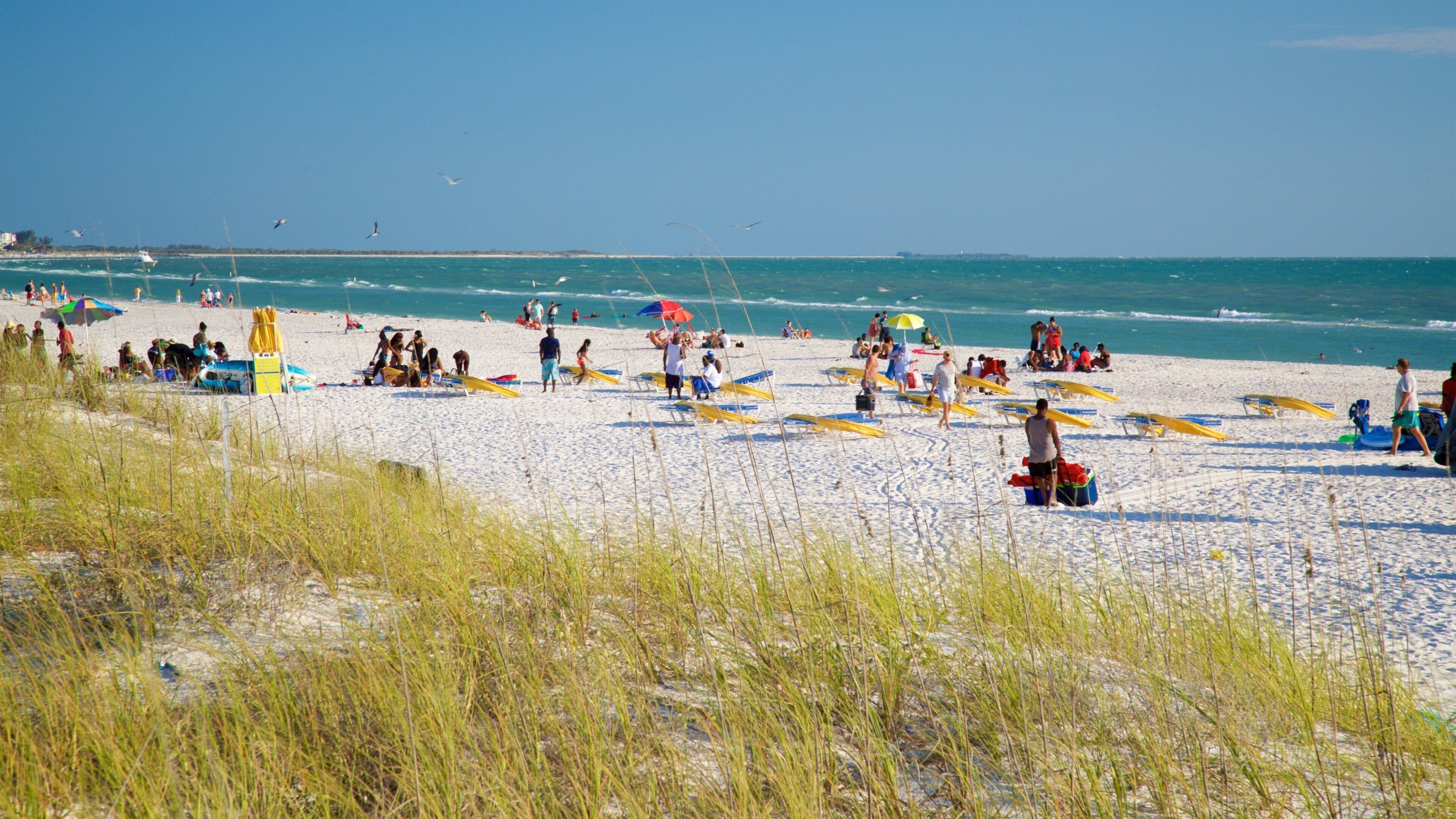 A crowded beach with people sunbathing, umbrellas, and boats.