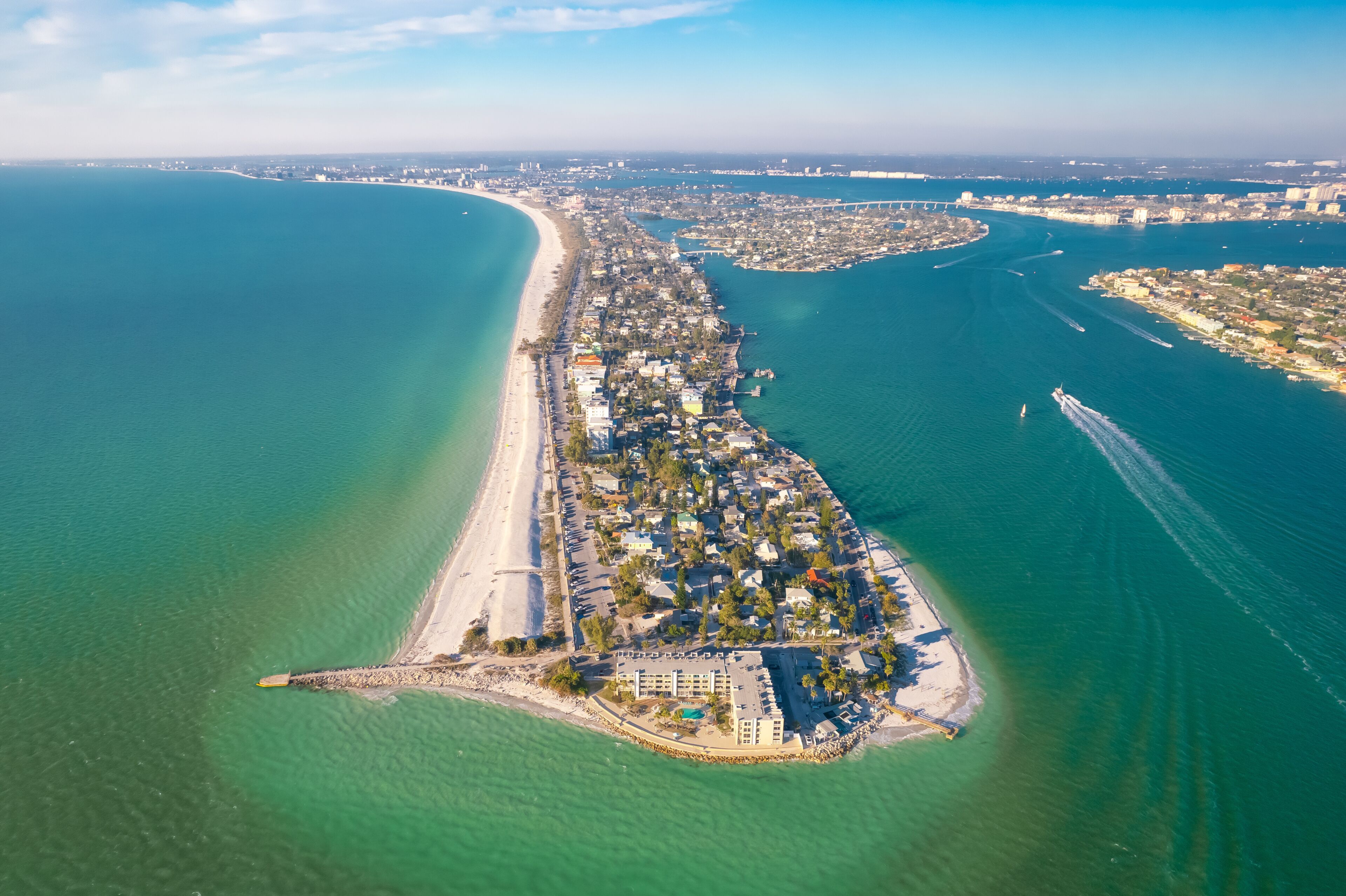 An aerial view of a coastal city with a long beachfront, a marina, and a bridge connecting two land masses.