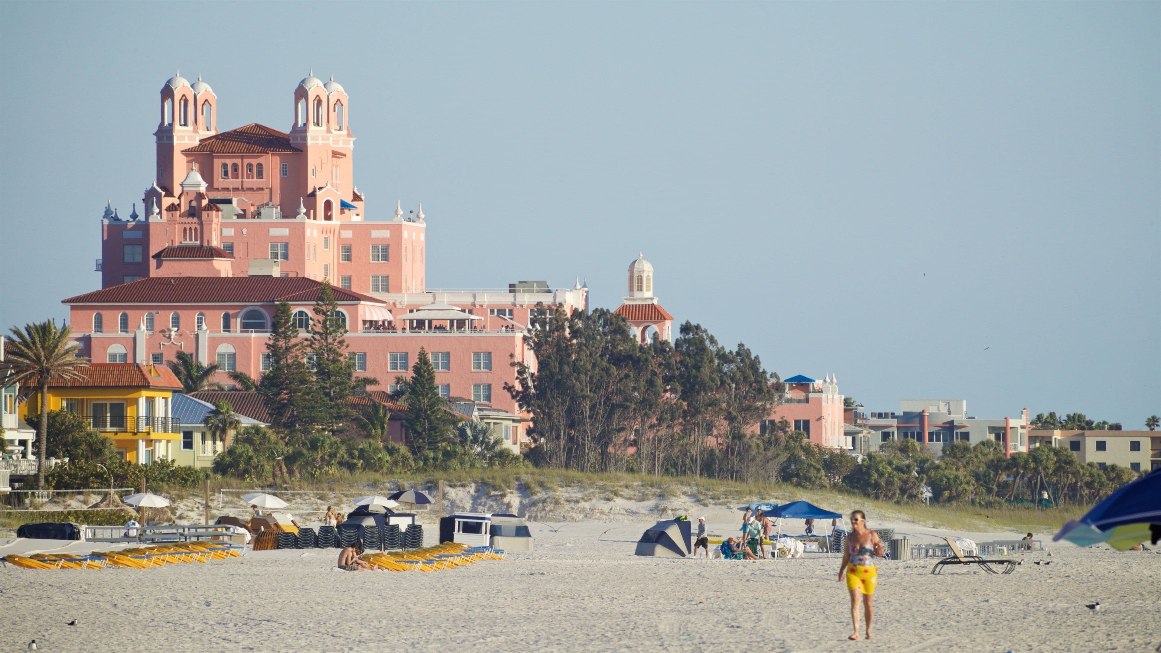 A beach with umbrellas, beach chairs, and a large pink building with towers.