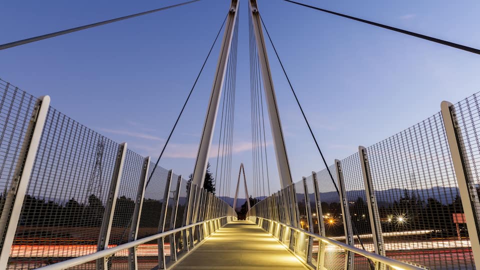 A suspension bridge at dusk with illuminated pathways and metal railings.