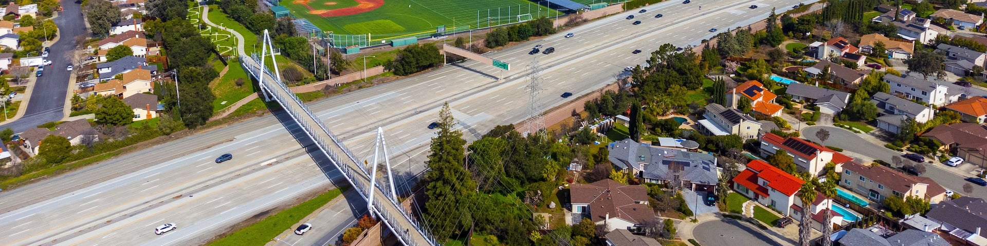Aerial view of a high school grounds in residential neighborhood near Don Burnett bicycle pedestrian cable-stayed bridge over Interstate 280, spanning Cupertino and Sunnyvale, California