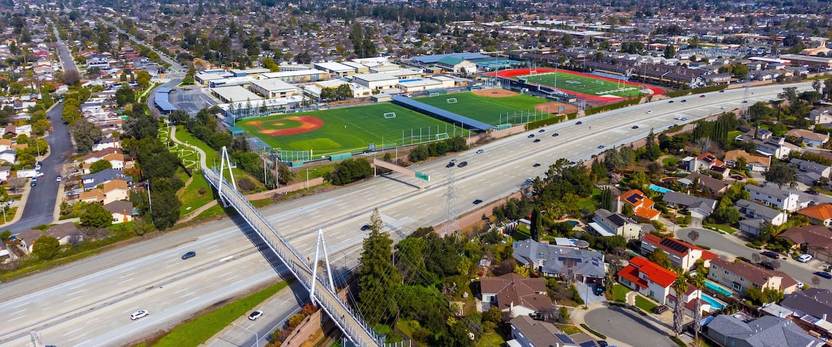 Aerial view of a high school grounds in residential neighborhood near Don Burnett bicycle pedestrian cable-stayed bridge over Interstate 280, spanning Cupertino and Sunnyvale, California
