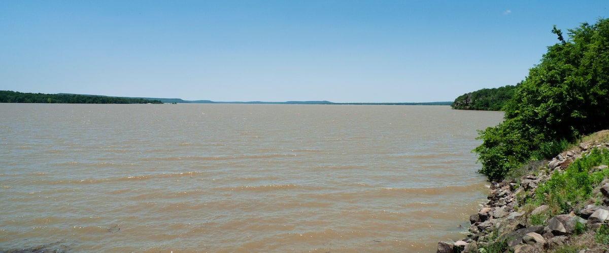 A river with a rocky shoreline and a forested area in the distance.