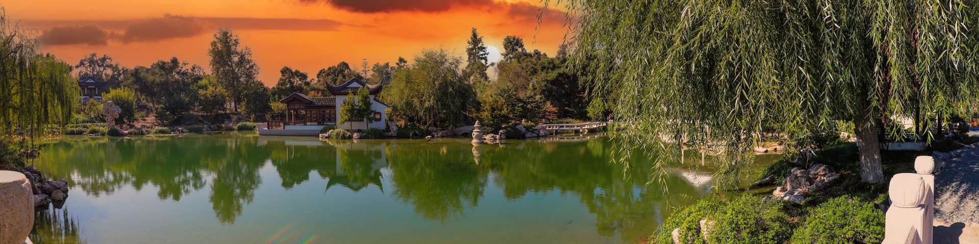 a stunning panoramic shot of a Japanese garden with deep green lake water and lush green trees reflecting off the lake with weeping willow trees powerful clouds at Huntington Library in San Marino