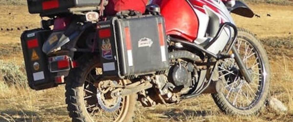 A red and white motorcycle with a sidecar parked on a grassy field with mountains in the background.