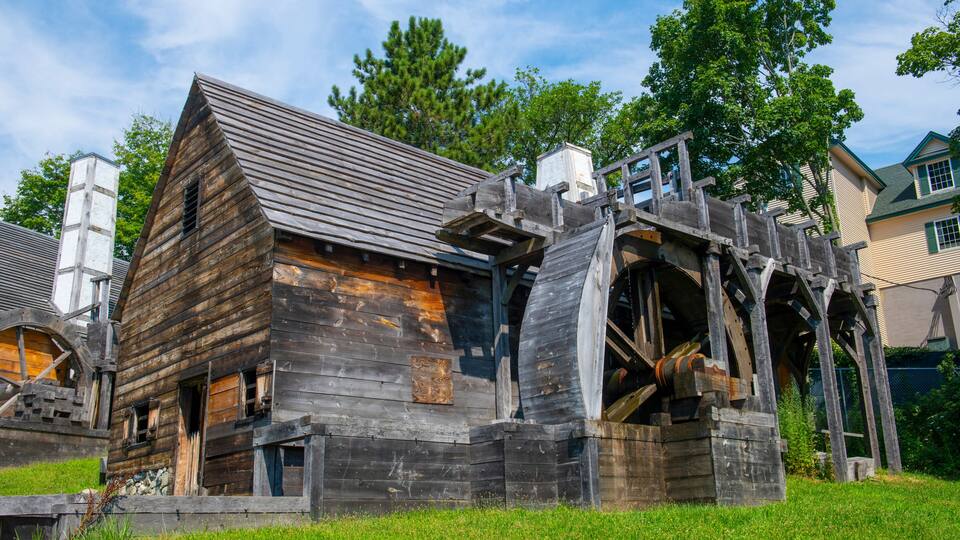 A rustic wooden building with a large water wheel and a wooden staircase.