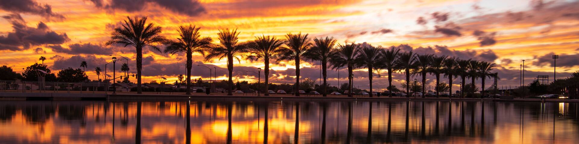 A sunset over a calm body of water with palm trees reflecting the sky.