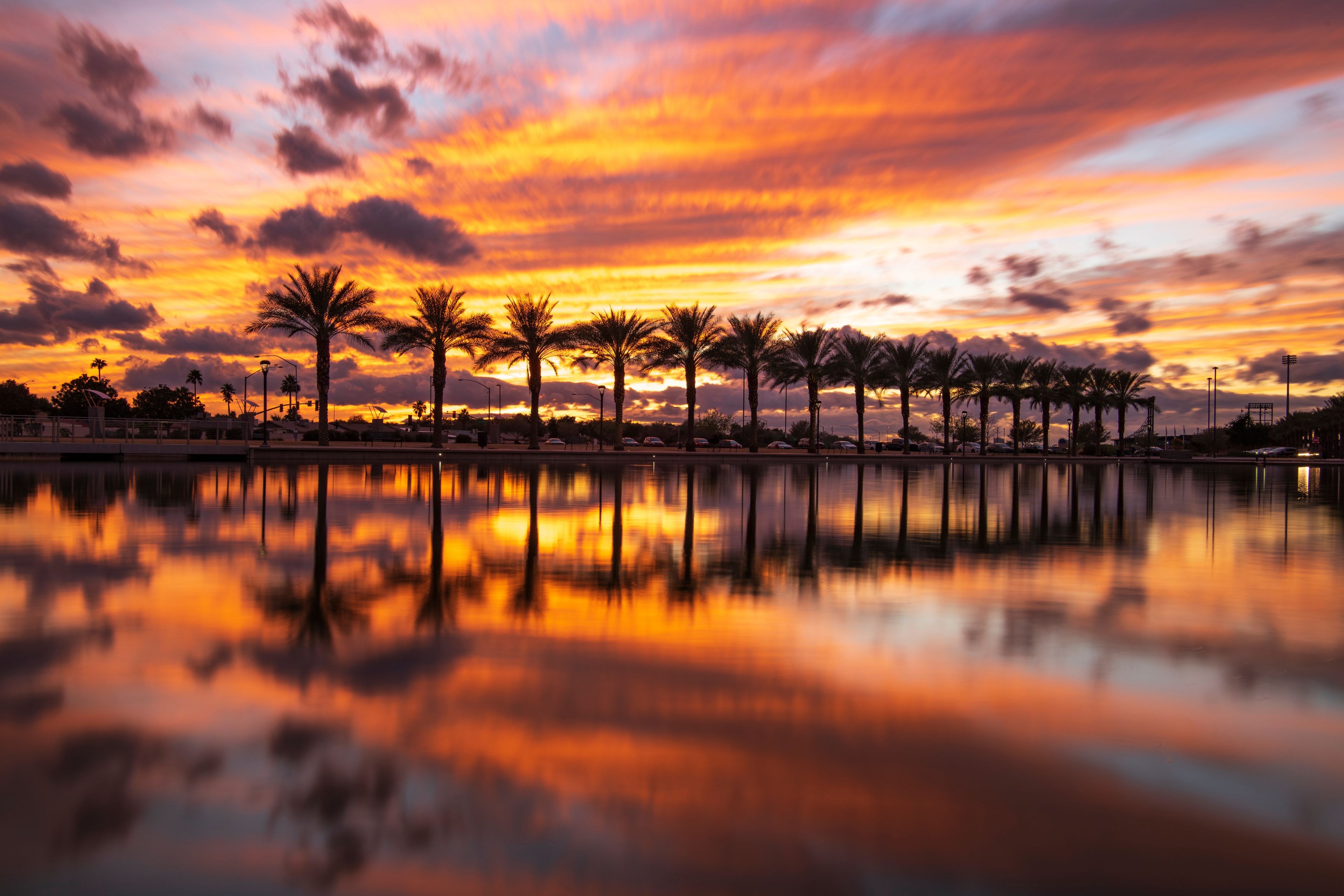 A sunset over a calm body of water with palm trees reflecting the sky.