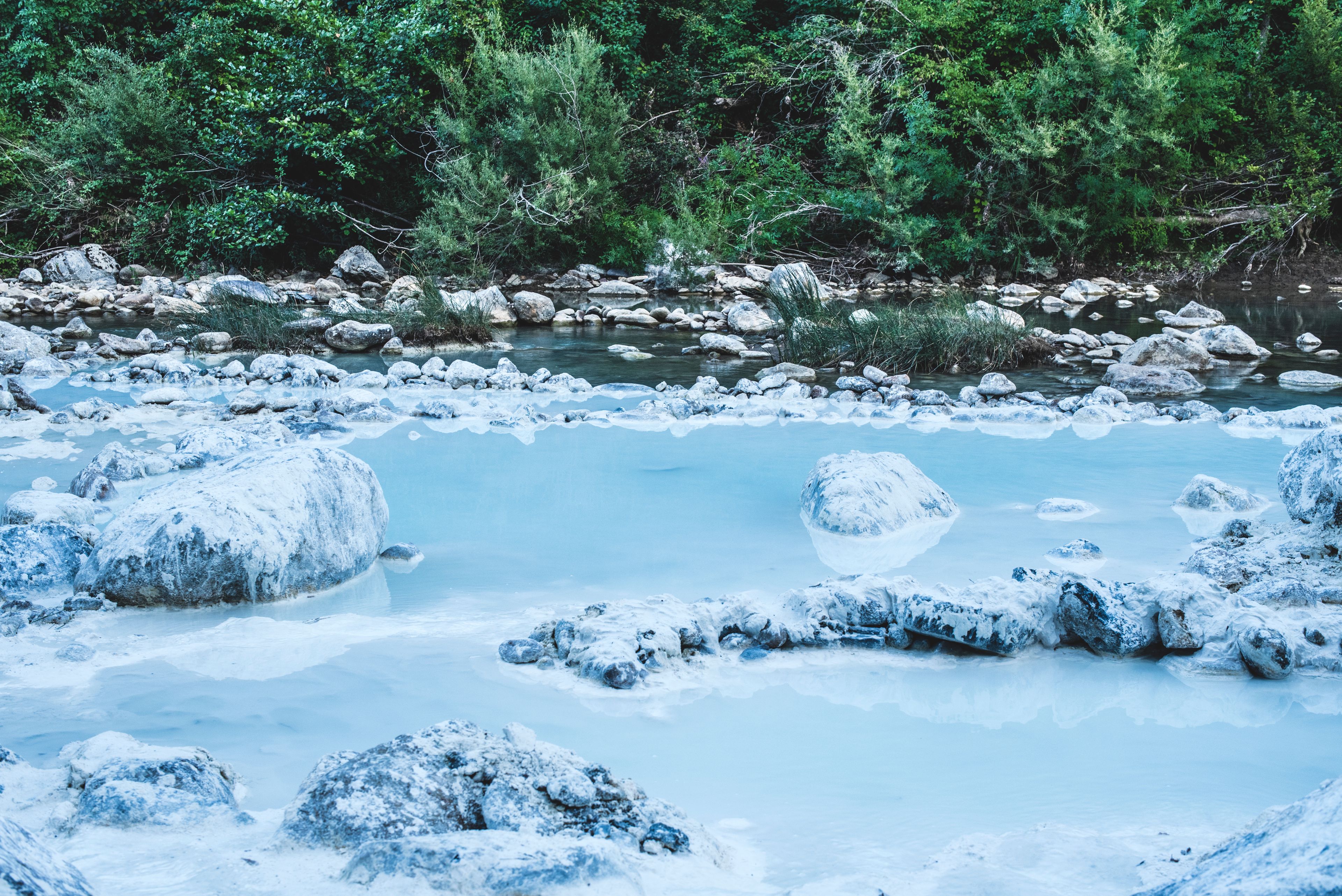 Un río de aguas cristalinas, rodeado de rocas y exuberante follaje verde.