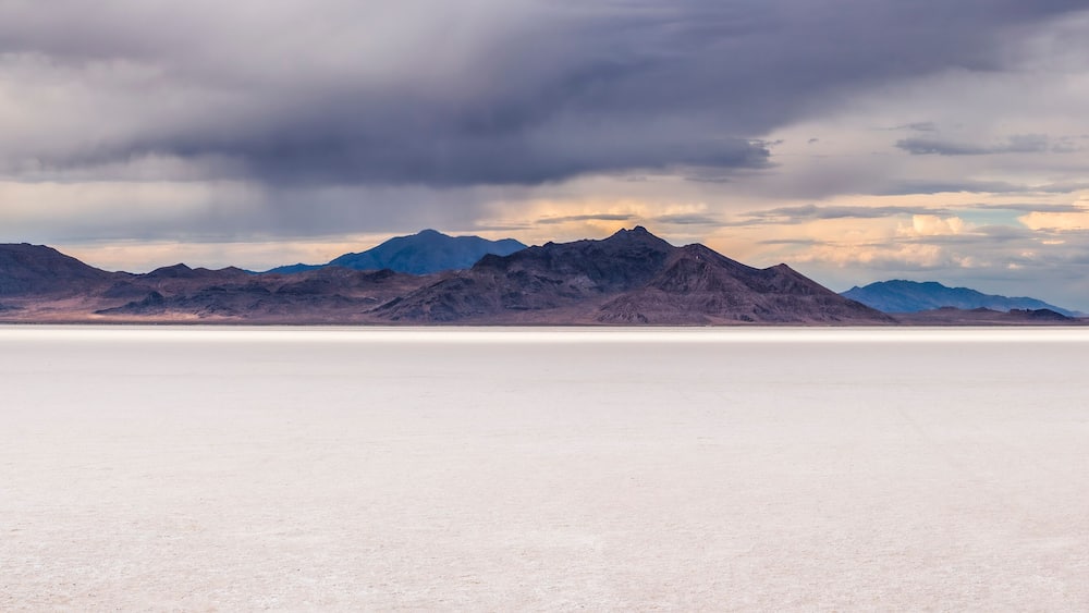 A vast salt flat with mountains in the background under a cloudy sky.