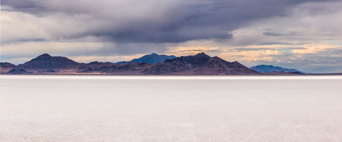 A vast salt flat with mountains in the background under a cloudy sky.