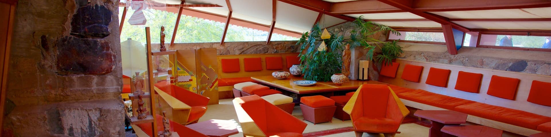 A modern interior with orange and red furniture, a stone wall, and a wooden ceiling.