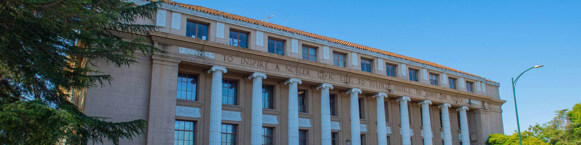 A large classical building with columns, a grand staircase, and a clear blue sky.