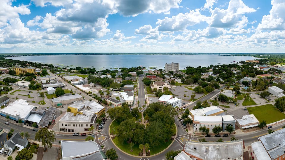 A coastal cityscape with a large body of water, dense greenery, and a mix of residential and commercial buildings.