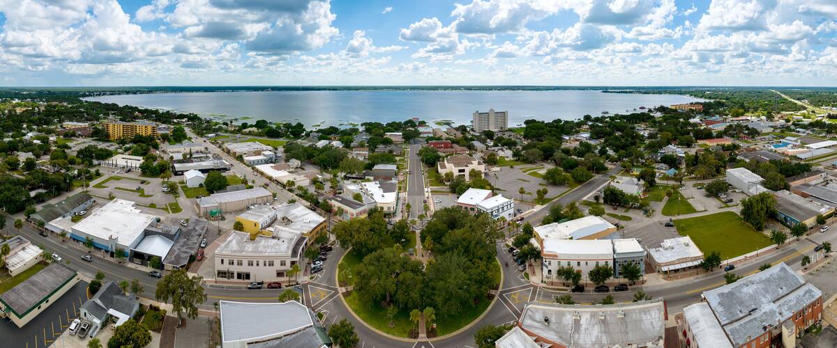 A coastal cityscape with a large body of water, dense greenery, and a mix of residential and commercial buildings.