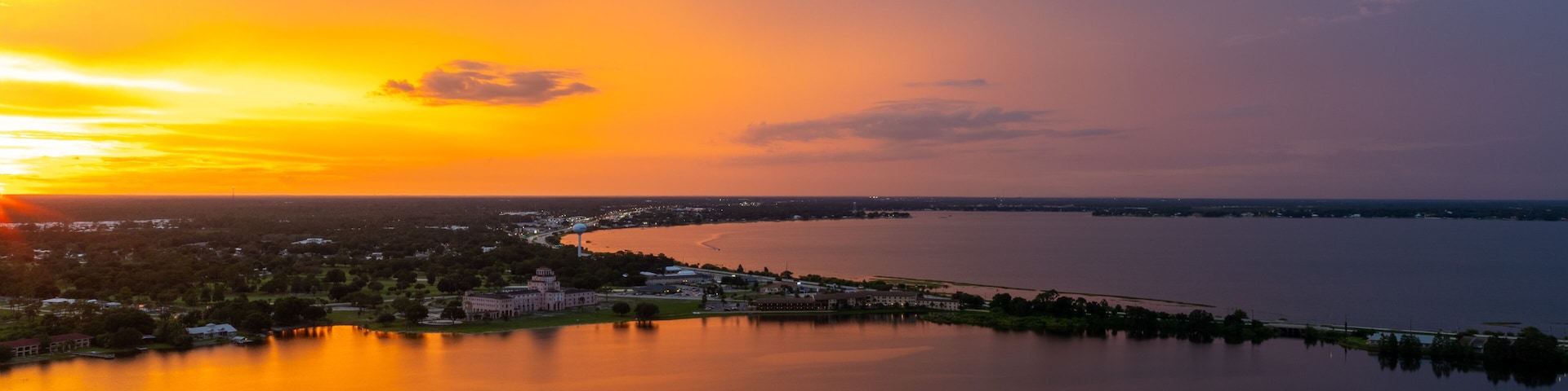 Un atardecer sobre un lago tranquilo con un paisaje urbano a lo lejos.