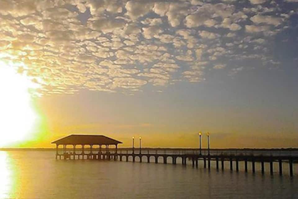 Un muelle se adentra en aguas tranquilas al atardecer, con el sol bajo en el horizonte.