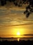 Auringonlasku vesistön yllä, jossa näkyy puiden siluetteja ja kaupungin siluetti kauempana horisontissa.