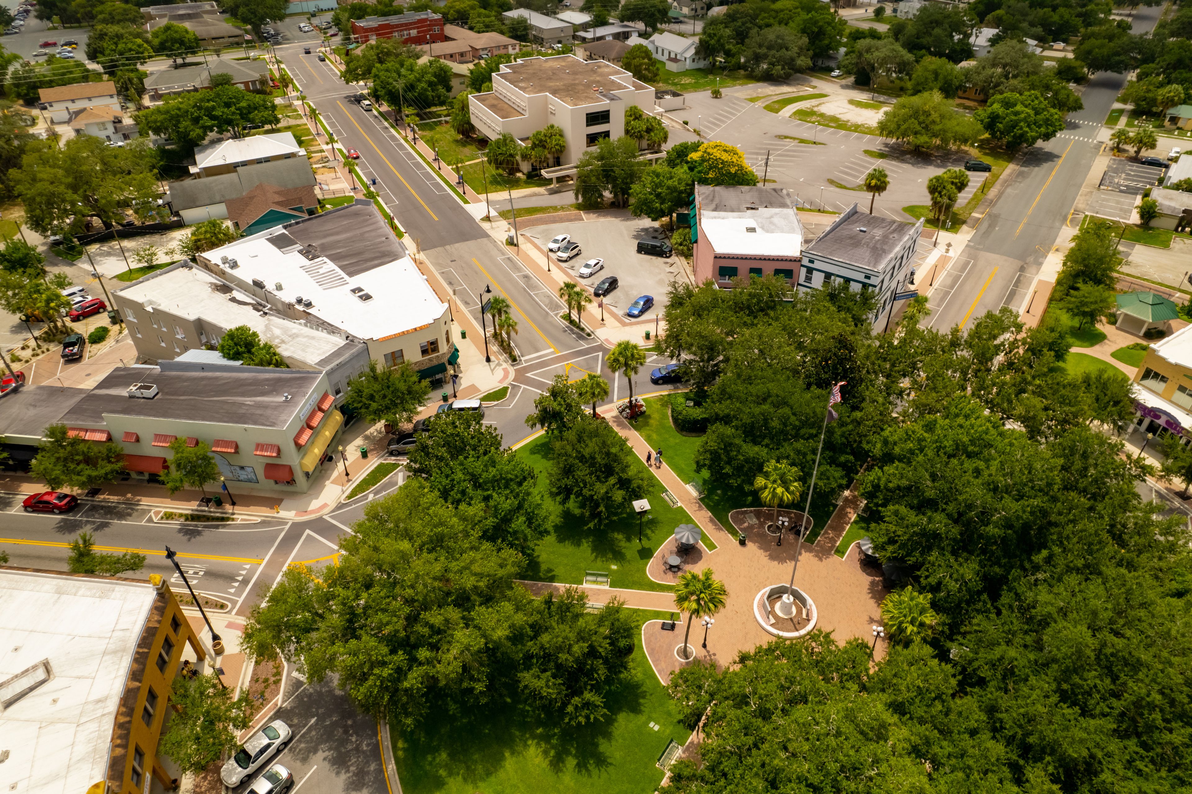 An aerial view of a town with a central roundabout, green spaces, and various buildings.