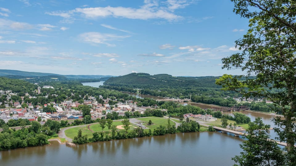 A town by a river with a bridge, surrounded by hills and greenery.