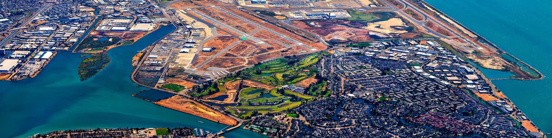 An aerial view of a coastal city with a dense urban area, a large body of water, and a mix of industrial and green spaces.