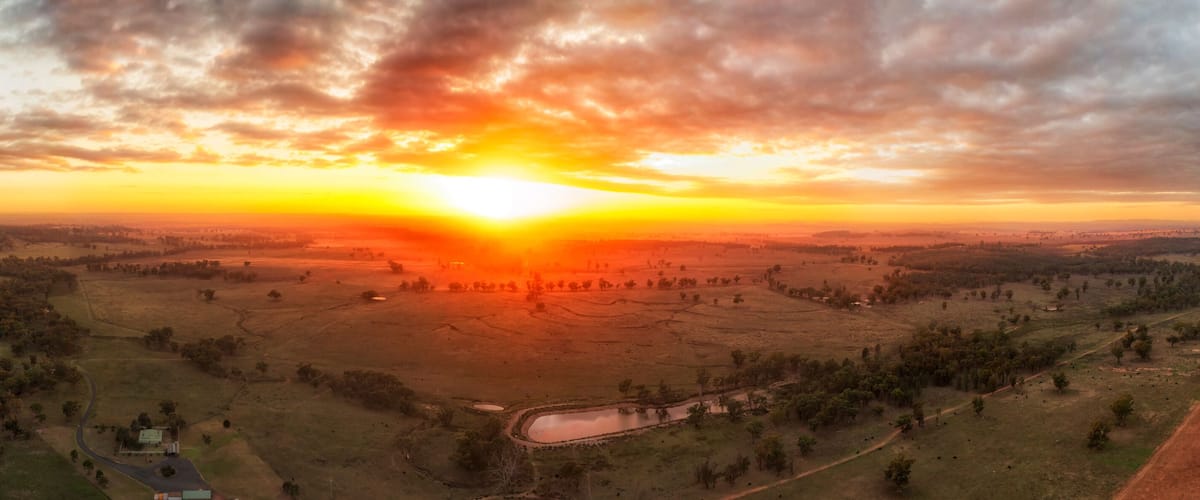 A sunset over a rural landscape with fields, a winding road, and a small body of water.