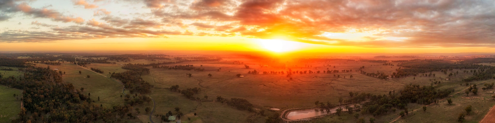 A sunset over a rural landscape with fields, a winding road, and a small body of water.