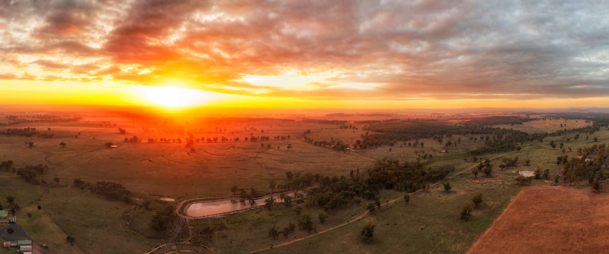 A sunset over a valley with fields, a small body of water, and scattered trees.