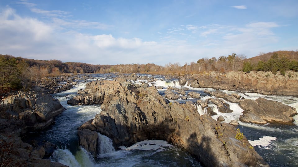 A river flowing through a rocky gorge with waterfalls and a forested hillside in the background.