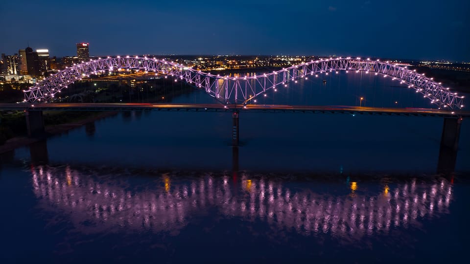 A bridge with purple lights reflecting on the water at night.