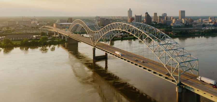 A steel arch bridge over a river with a city skyline in the background.