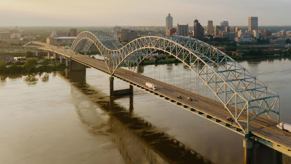 A steel arch bridge over a river with a city skyline in the background.