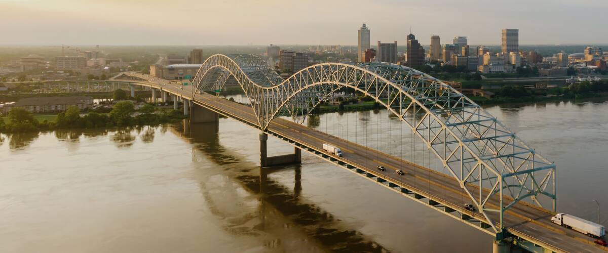 A steel arch bridge over a river with a city skyline in the background.
