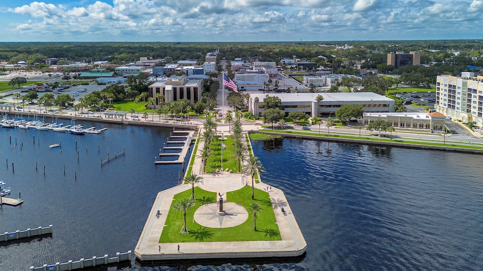 A marina with boats docked, a central island with a monument, and surrounding buildings.