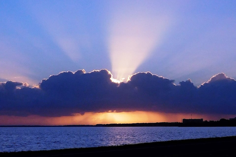 A sunset over a body of water with clouds silhouetted against the sky.