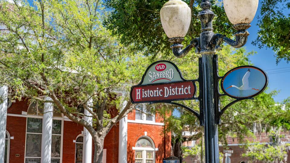 A historic district sign with a white bird symbol, a brick building, and a street lamp.